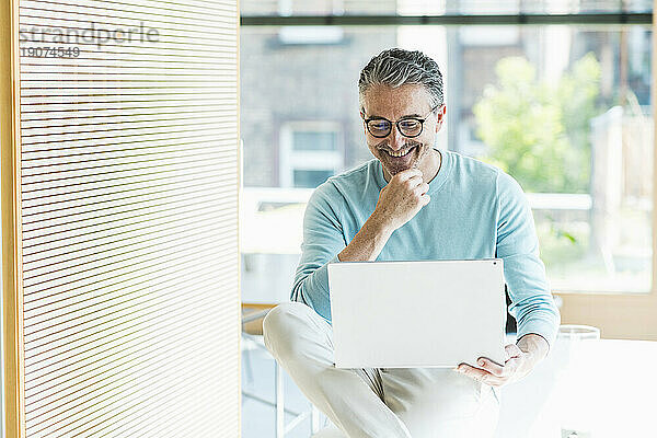 Glücklicher Geschäftsmann  der im Büro am Laptop arbeitet