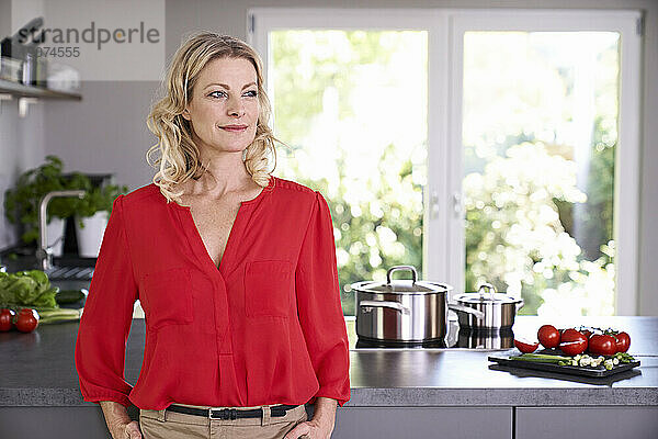 Selbstbewusste Frau in roter Bluse steht in der Küche