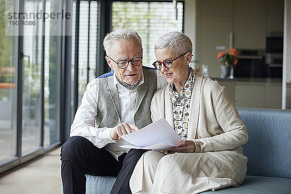 Senior couple sitting on couch at home reading document