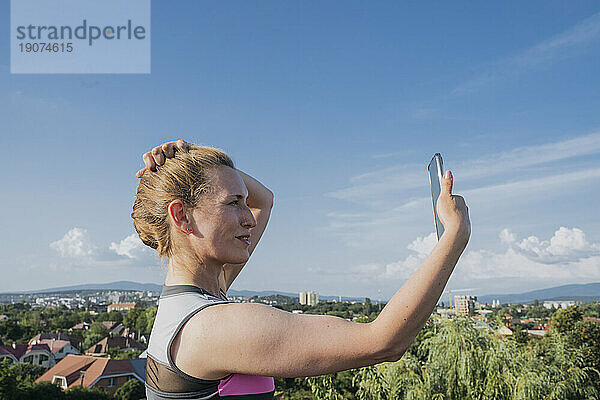 Lächelnde Frau macht Selfie unter blauem Himmel