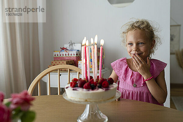 Lächelndes Mädchen  das zu Hause hinter Kuchen mit Kerzen steht