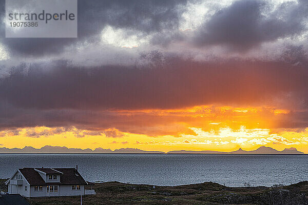 Einsames traditionelles Haus am Meer unter einem dramatischen Himmel im Morgengrauen  Reine  Lofoten-Inseln  Nordland  Norwegen  Skandinavien  Europa