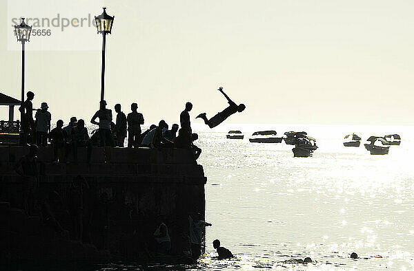 Silhouetted teenagers dive into the sea from the town pier  Stone Town  Zanzibar island  Tanzania  East Africa  Africa