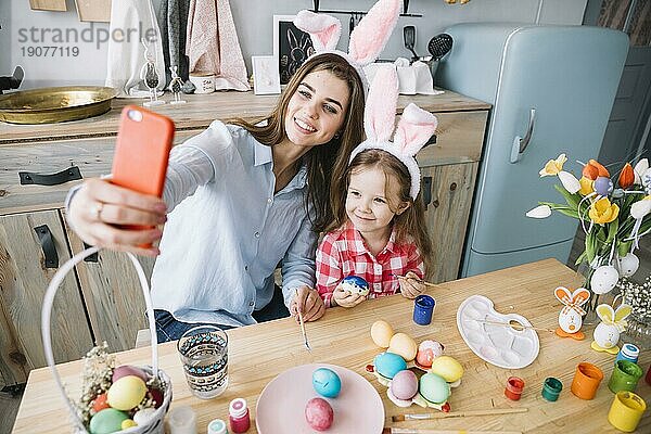 Junge Frau macht Selfie mit Tochter in der Nähe von Ostereiern