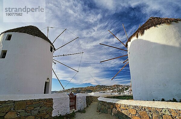 Berühmte Touristenattraktion von Mykonos  Kykladen  Griechenland. Zwei traditionelle  weiß getünchte Windmühlen am Wasser und die Stadt Chora mit ihrem Hafen. Sommer  blauer Himmel  schöne Wolken. Reiseziel  ikonische Ansicht. Rückansicht