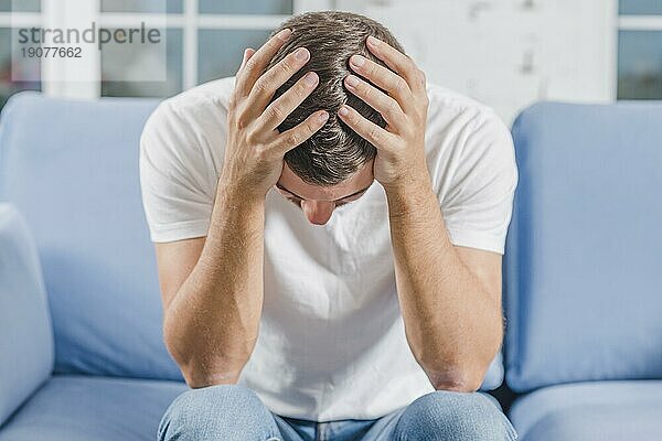 Frustrierter Mann mit Kopfschmerzen auf dem Sofa