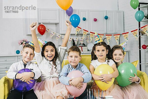 Porträt Kinder sitzen auf dem Sofa und halten Luftballons