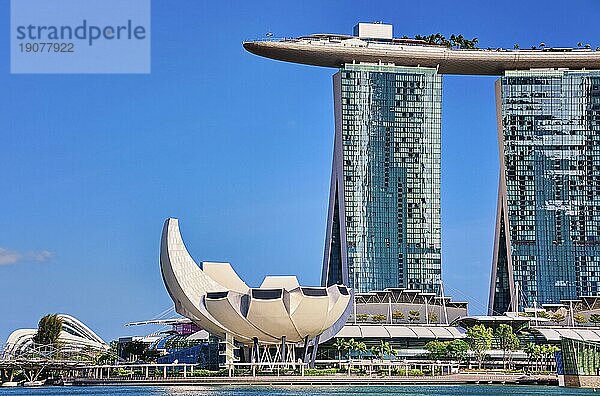 Singapur  25. Februar 2020. Berühmtes Touristenziel  Marina Bay Sands  Shoppes Einkaufszentrum  ArtScience Museum und Helixbrücke in der Marina Bay  an einem sonnigen Tag. Sehenswerte Wahrzeichen des Stadtstaates  klarer blauer Himmel  azurblaues Wasser. Ikonische futuristische Architektur und Symbole  Asien