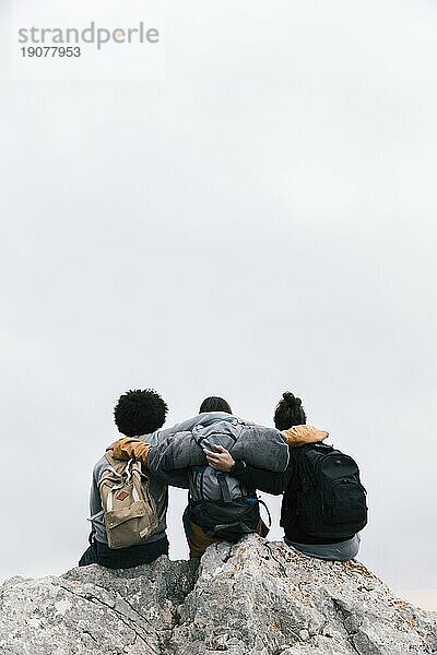 Drei Freunde mit ihren Armen um einen sitzenden Berg