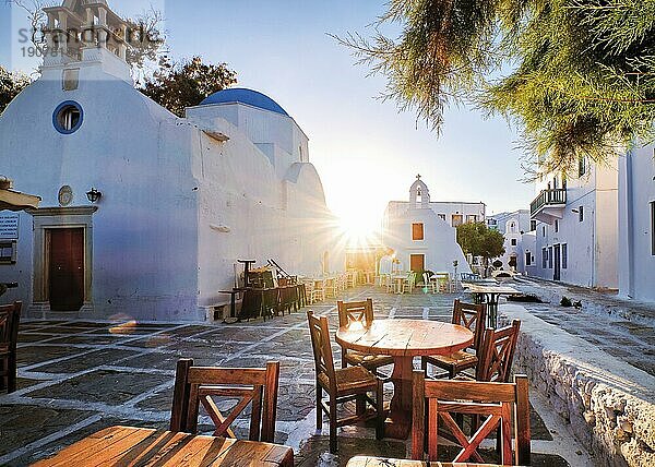 Sonnenaufgang in den Gassen des berühmten Reiseziels  Mykonos Insel  Griechenland. Griechische weiß getünchten Kirchen in der kleinen Stadt Platz  Straße Cafe Tische und Stühle  Sonne und Objektiv Flares. Urlaub  Entspannung im Mittelmeer  Kykladen und Ägäische Inseln