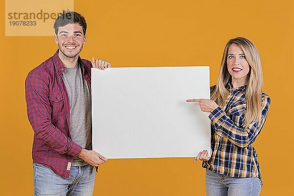 Junge Frau zeigt mit dem Finger Plakat von seinem Freund gegen orange Hintergrund halten