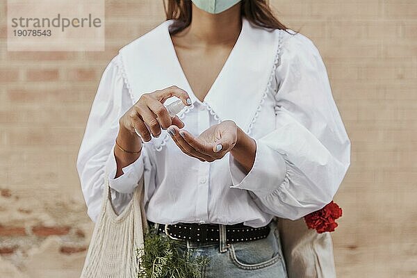 Frontansicht einer Frau mit Gesichtsmaske bei der Anwendung von Handdesinfektionsmitteln