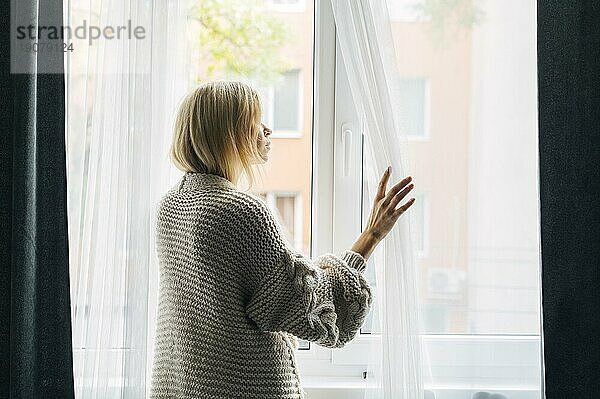 Seitenansicht melancholische Frau zu Hause während der Pandemie mit Blick durch das Fenster