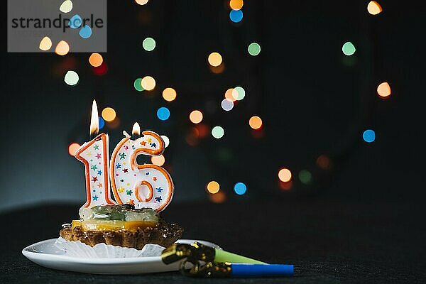 Nummer 16 Geburtstag beleuchtete Kerze Scheibe Torte mit Partei Horn Blower gegen beleuchtete Bokeh Hintergrund