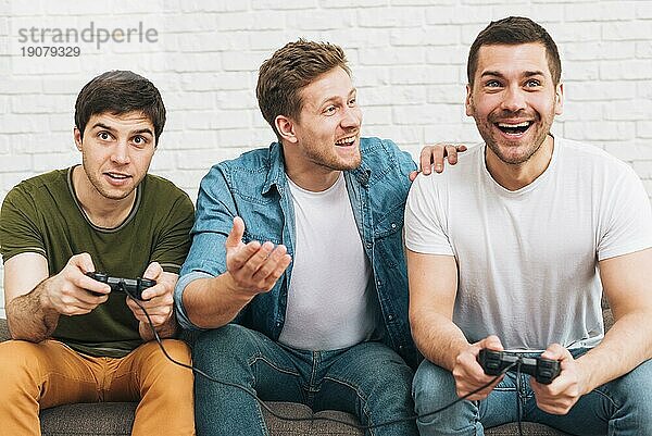 Drei männliche Freunde sitzen zusammen und genießen ein Videospiel