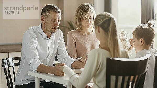 Schöne Familie betet vor dem Essen