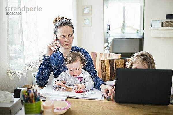 Frau spricht mit Smartphone  während ihre Kinder am Schreibtisch spielen