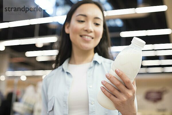 Fröhliche asiatische Frau hält Flasche Milch Supermarkt