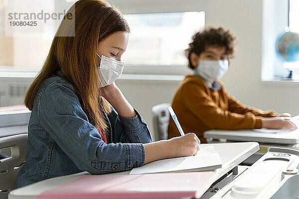 Seitenansicht Kinder mit medizinischen Masken im Klassenzimmer beim Lernen