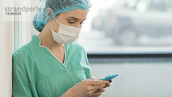 Seitenansicht Krankenschwester mit Maske bei der Kontrolle des Handys