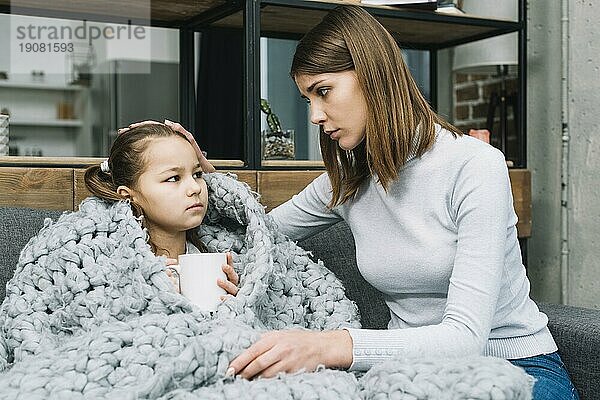 Mutter kümmert sich um ihre Tochter  die mit einem grauen Wollschal bedeckt ist und an Fieber leidet