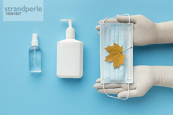 Draufsicht Hände halten medizinische Maske mit Herbstblatt flüssige Seife Flasche