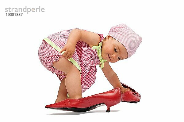 Lustige adorable Baby Mädchen Dame versuchen auf einem großen roten Frauen Schuhe  vor weißem Hintergrund