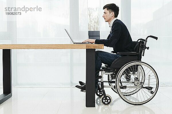 Seitenansicht junger Geschäftsmann im Rollstuhl sitzend mit Laptop neues Büro