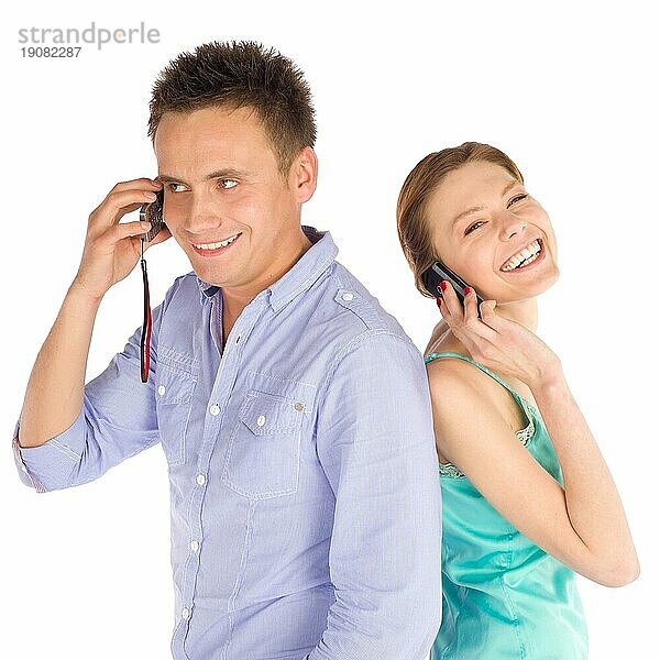Junges glückliches lächelndes Paar  das Rücken an Rücken steht und telefoniert  vor weißem Hintergrund