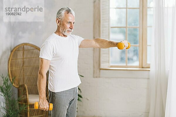 Fitter älterer Mann  der mit orangefarbenen Hanteln zu Hause trainiert