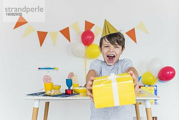 Fröhlicher Junge nimmt gelbe Geschenkbox mit weißem Band