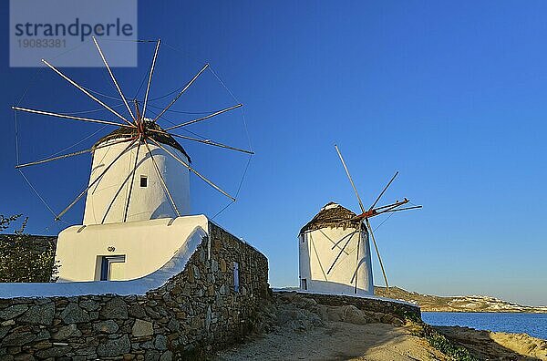 Berühmte Touristenattraktion von Mykonos  Kykladen  Griechenland. Zwei traditionelle weiß getünchte Windmühlen am Wasser und die Stadt Chora. Sommer  Morgen  klarer blauer Himmel  Reiseziel  ikonische Ansicht. Frontalaufnahme