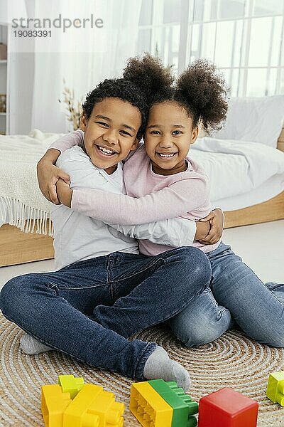 Vorderansicht zwei lächelnde Geschwister  die sich zu Hause umarmen