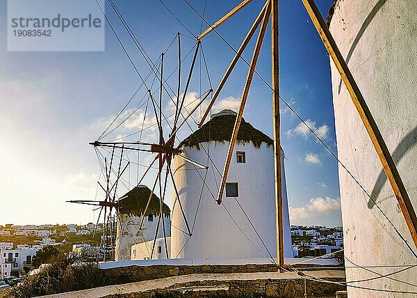 Berühmte Touristenattraktion von Mykonos  Kykladen  Griechenland. Drei traditionelle weiß getünchte Windmühlen in einer Reihe gegen die aufgehende Sonne über Chora  dem Hauptort der Insel. Sommer  Morgen  blauer Himmel  Wolken. Reiseziel  ikonische Ansicht