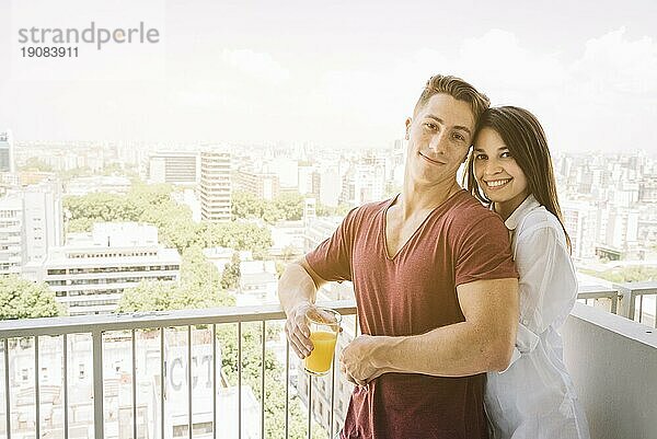 Glückliche Frau umarmt Mann mit Saftglas Balkon
