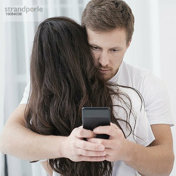 Mann  der seine Freundin umarmt  während er sein Handy überprüft
