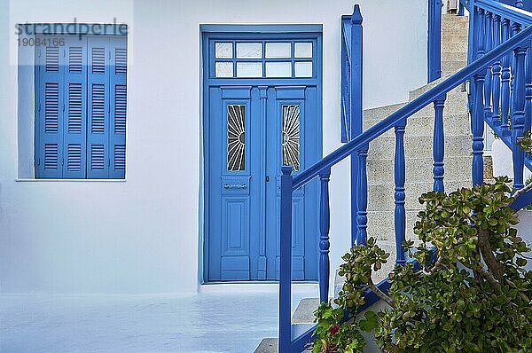 Traditionelle griechische Haustür  weiß getünchte Wände  blaue Fensterläden  Eingangstür und Türen  Geländer der Straßentreppe. Mittelmeer  griechische Inseln  einzigartiges Design  ägäischer oder kykladischer Stil. Europa  Architektur  Details  Design. Frontalaufnahme