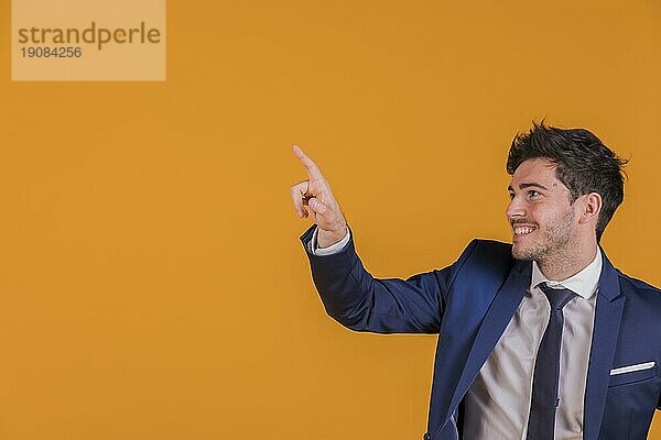 Porträt eines jungen Geschäftsmannes  der mit dem Finger auf einen orangefarbenen Hintergrund zeigt