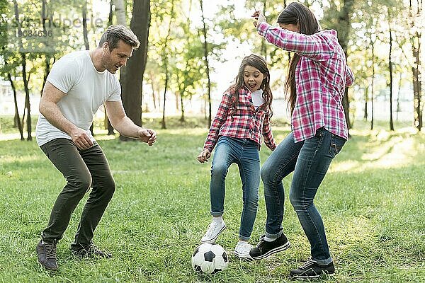 Fröhliches Mädchen spielt Fußball mit ihren Eltern im Park
