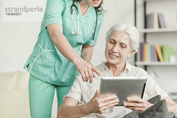 Krankenschwester zeigt etwas älteren weiblichen Patienten digitale Tablette