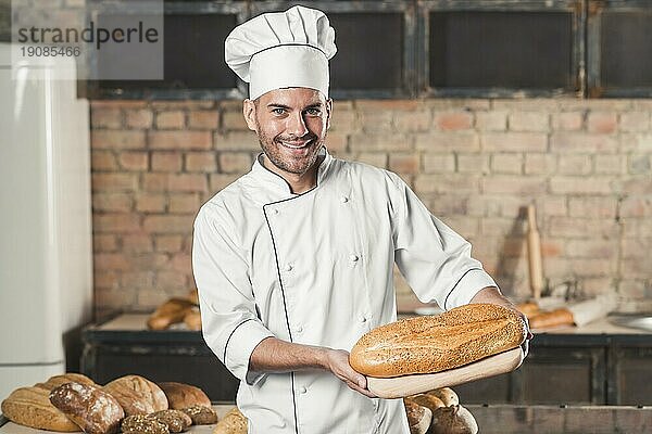 Lächelnder männlicher Bäcker mit Schneidebrett für gebackenes Brot