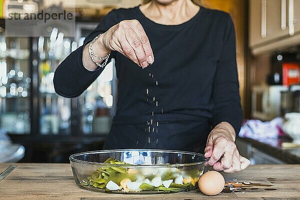 Crop Hände ältere Frau bestreuen Gericht Salz