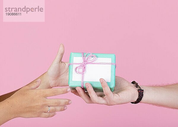Mann s Hand geben Geschenkbox andere Person gegen rosa Hintergrund