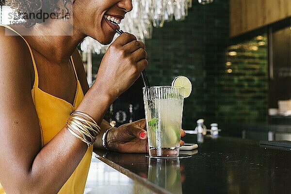 Lächelnde junge Frau trinkt Mojito am Tresen eines Restaurants