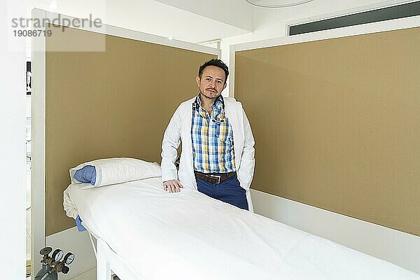 Latino Arzt posiert neben einem Tisch in seinem Schönheitszentrum