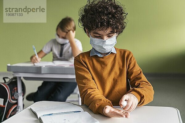 Vorderansicht Kind mit medizinischer Maske beim Desinfizieren der Hände Klasse