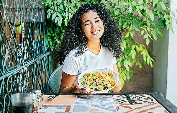 Schönes Mädchen sitzt und hält einen Caesar Salat. Porträt eines lächelnden Mädchens  das Caesarsalat isst. Konzept der gesunden Ernährung und gesundes Leben