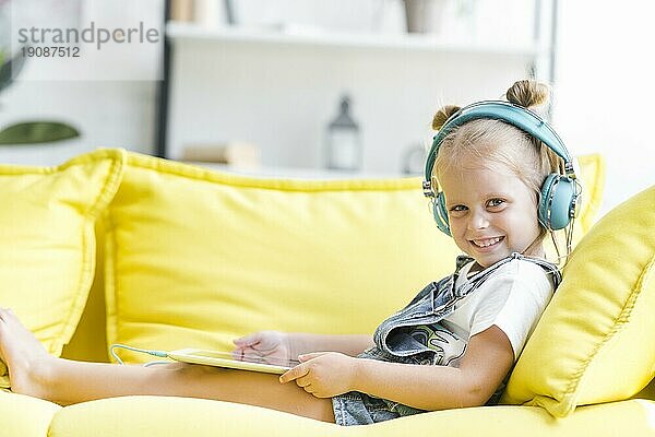 Lächelndes süßes kleines Mädchen Kopfhörer hören Musik mit Tablet