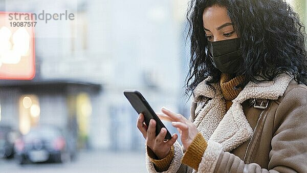 Frau mit medizinischer Maske überprüft ihr Telefon