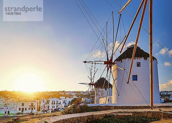 Berühmte Touristenattraktion von Mykonos  Kykladen  Griechenland. Drei traditionelle weiß getünchte Windmühlen in einer Reihe gegen die aufgehende Sonne über Chora  Hauptort der Insel. Sommer  Sonnenaufgang  Morgen  blauer Himmel  Wolken. Reiseziel  ikonische Ansicht